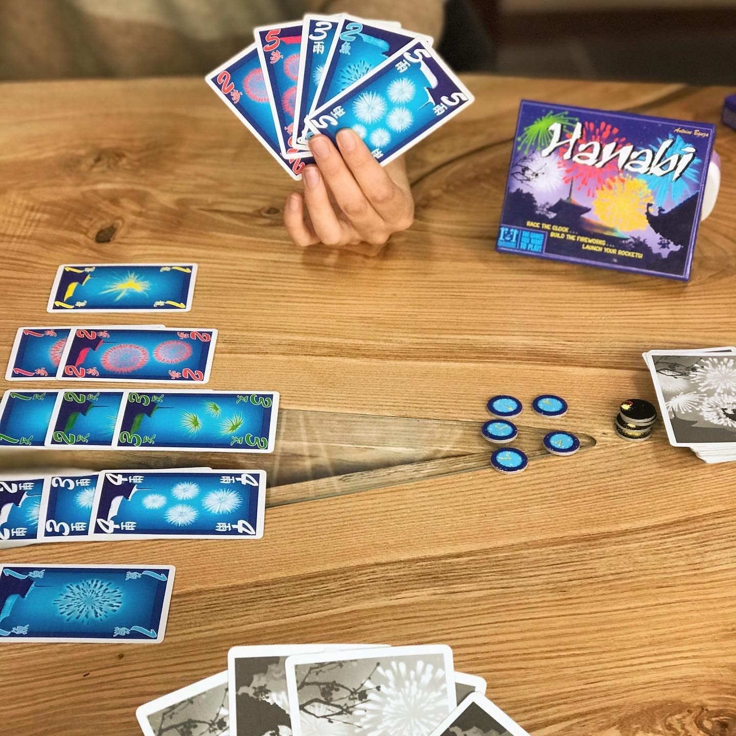 A scene of people playing the card game Hanabi. The cards have colors and suits representing fireworks.